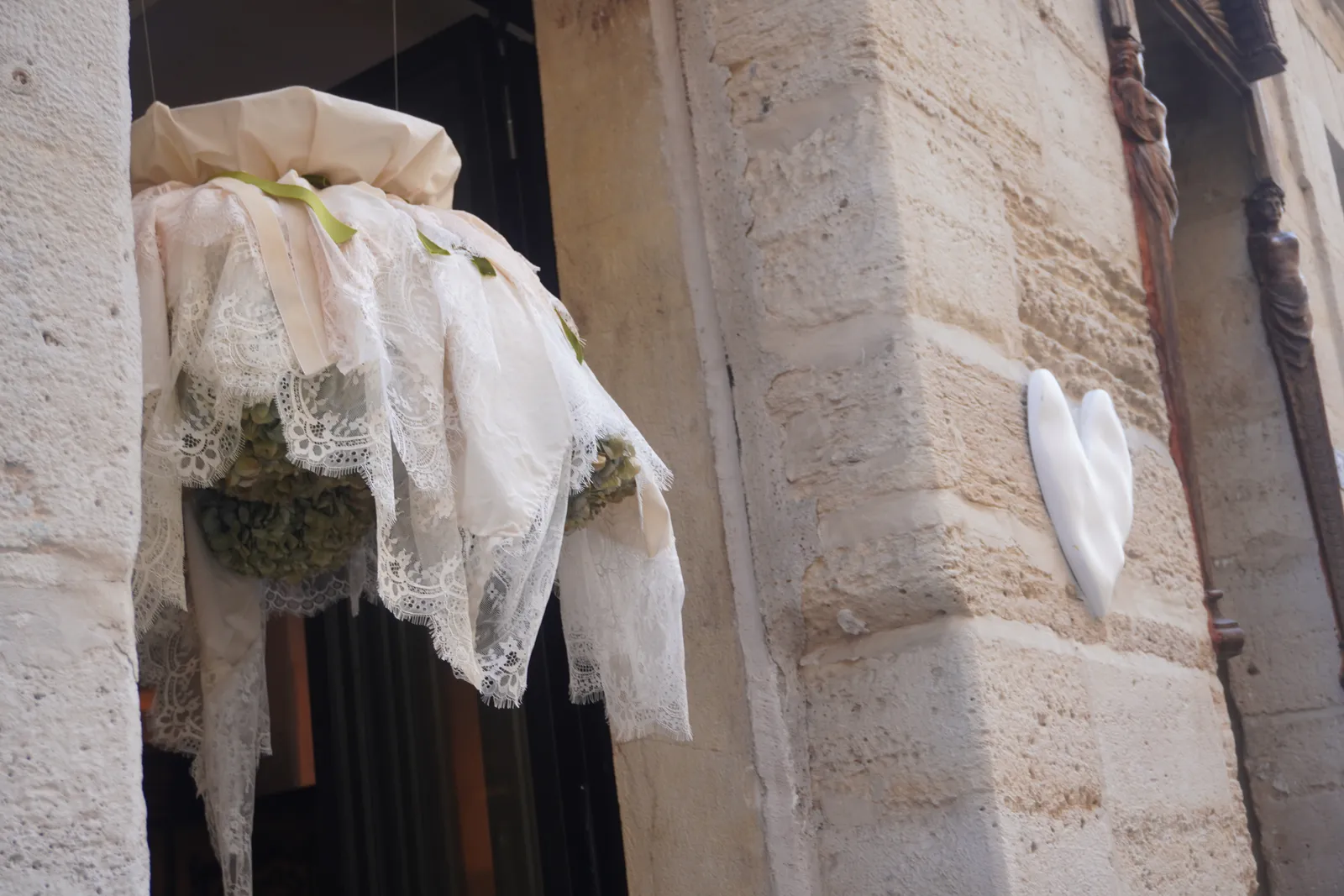 The white stone heart set into the old stone corner at 7 by Sevenly Heart, beside a hanging veil of lace and dried flowers.