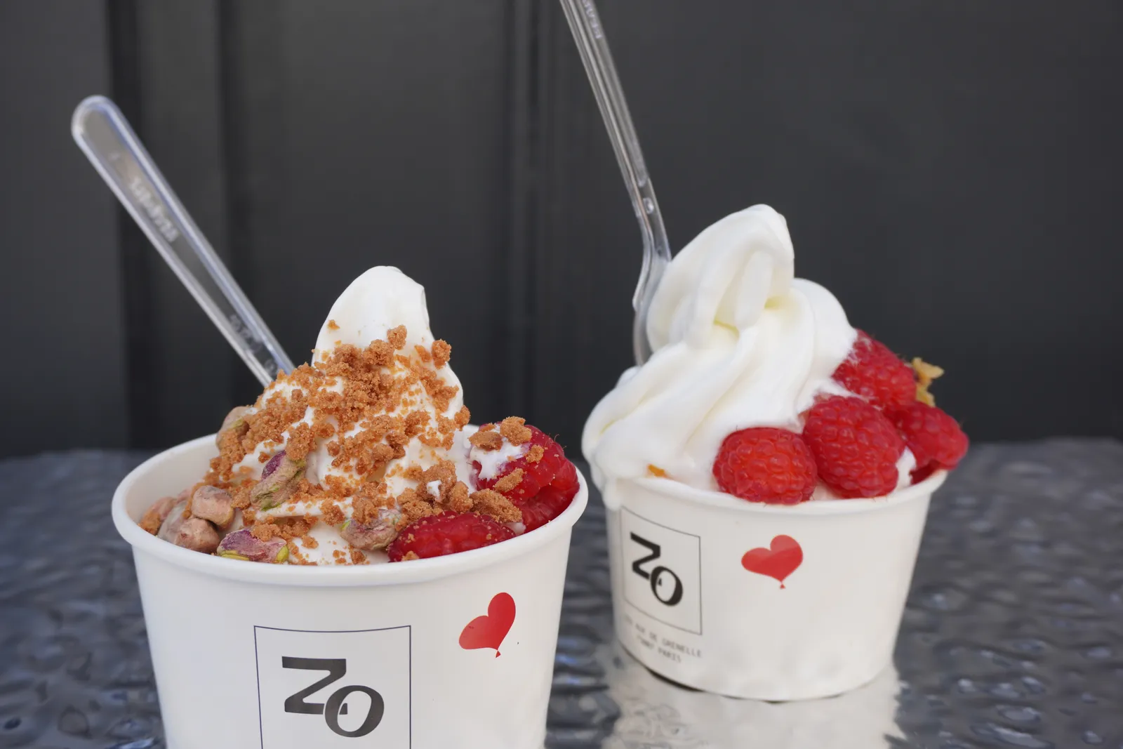 Two Café Zo cups with the Zo mark and a small red heart, soft-serve topped with raspberries, pistachio and cookie crumble.